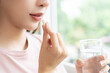 © KMPZZZ - Sick, asian young woman, girl hand holding pill capsule, painkiller medicine from stomach pain, head ache, pain for treatment, take drug or vitamin and glass of water at home, pharmacy and health care