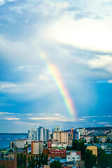 Beautiful multicolored rainbow in the blue sky above the city. Vertical photo.