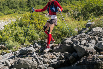 Wall Mural - woman athlete with trekking poles in hands descend stones trail  in mountain marathon