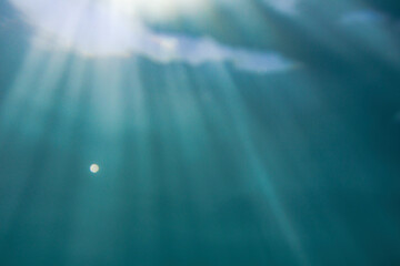 Air bubbles and light beams fall through the surface of the sea into the blue green water