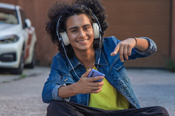 Canvas Print - Young man with headphones enjoying music sitting on the street