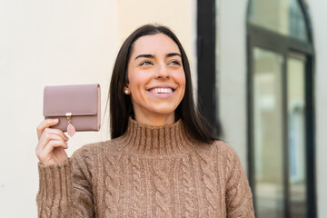 Poster - Young woman holding a wallet at outdoors looking up while smiling