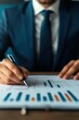 © Jammy - Businessman analyzing financial data and graphs with a pen. Professional setting focusing on performance and strategy.