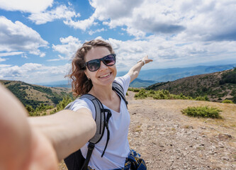 Young woman traveler walking in summer mountains taking selfie while hiking