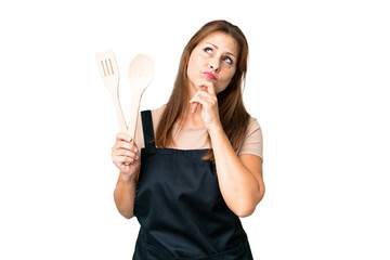 Middle age caucasian woman holding a rolling pin over isolated background and looking up