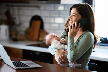 Wall Mural - Stay at home mom working remotely on laptop while taking care of her baby. Global work on computer