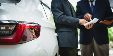 Wall Mural - Two Asian individuals discuss a car insurance claim with an agent in front of a damaged vehicle. They review documents, discuss the policy, and address the crash and repair costs.