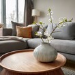 © Stefan - Close up of ceramic vase with blossom twigs on round wooden coffee table against grey sofa and window. Minimalist home interior design of modern living room.