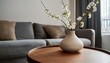 © Stefan - Close up of ceramic vase with blossom twigs on round wooden coffee table against grey sofa and window. Minimalist home interior design of modern living room.