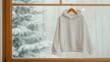 © Bantita - Blank hoodie hanging on a peg, snow-dusted window, Christmas candlelight scene