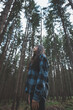 © Fauren - Happy woman in a plaid shirt enjoying the serenity of a dense forest, surrounded by tall trees, feeling freedom and connection with nature