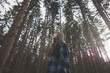 © Fauren - Happy woman in a plaid shirt enjoying the serenity of a dense forest, surrounded by tall trees, feeling freedom and connection with nature