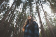 © Fauren - Happy woman in a plaid shirt with outstretched arms enjoying the serenity of a dense forest, surrounded by tall trees, feeling freedom and connection with nature