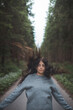 © Fauren - Young woman with flowing dark hair stands confidently on a forest road, her hair lifted by the wind. A blend of freedom, nature, and youthful energy captured in a serene woodland setting