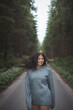 © Fauren - Young woman with flowing dark hair stands confidently on a forest road, her hair lifted by the wind. A blend of freedom, nature, and youthful energy captured in a serene woodland setting