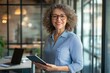© YURIMA - The image shows a confident businesswoman in a modern office, highlighting corporate creativity and leadership while using technology like a tablet to boost productivity and collaboration