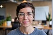 © Lull - Smiling woman office. Young woman with short hair, wearing glasses, smiles at the camera in an office setting.