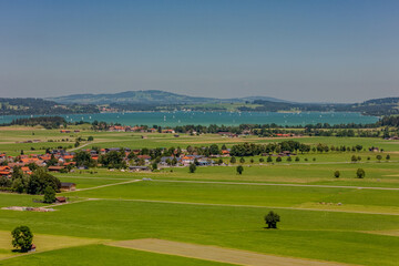 Scenic view of lush green fields and sparkling lake under a clear blue sky in Bavaria during a sunny afternoon