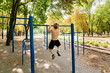 © Roman - View from the back as a teenager in the park pulls himself up on the bar.  Athletic teenage boy in the park outdoor workout session