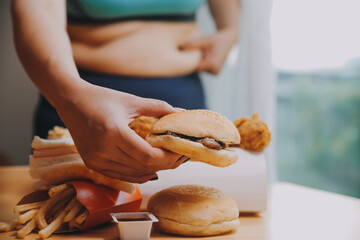 To eat or not. Cheerless plump woman looking at the burger while thinking to eat it or not