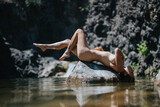 Artistic nude model reclines on a rock in a tranquil nature setting, embracing natural beauty and serenity.