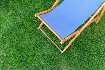 Deck chair with blue fabric on green grass background.