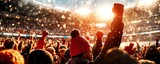 Excited crowd at a sports event celebrating with raised fists in the air, illuminated by a stunning sunset glow.