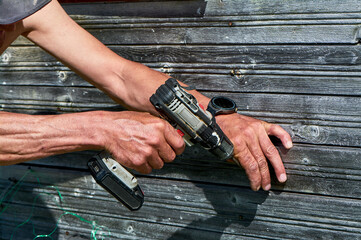 A man is using a power drill to make a hole in a wooden board