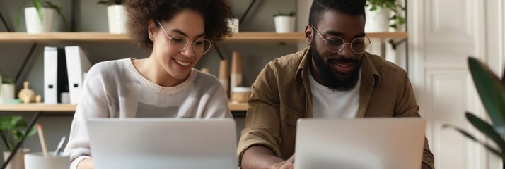 Two people are sitting at a table with two laptops in front of them. They are smiling and seem to be enjoying their time together