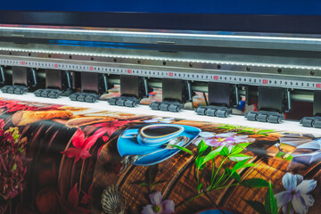 Leinwandbilder - A large printer is printing a colorful image of a coffee cup and flowers. The image is vibrant and lively, with a sense of warmth and comfort