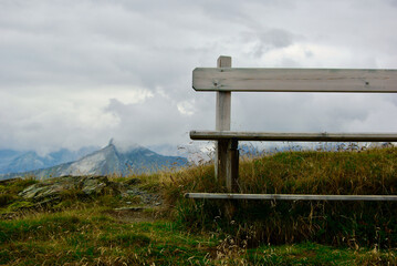Wall Mural - close-up of a wooden bench with a view of an amazing mountain landscape on a hazy day with gray clou