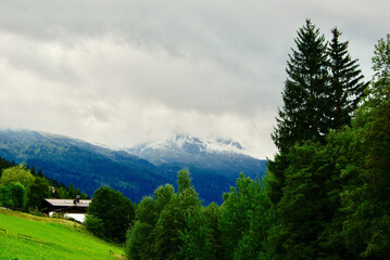 Wall Mural - view of a mountain landscape with a building on the hillside on a rainy day with gray clouds and fog