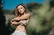 © qunica.com - A serene and confident woman standing outdoors in nature with her arms crossed, basking in the warm sunlight.