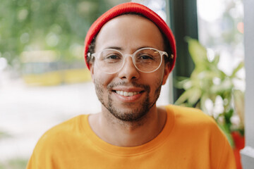 Young, smiling latin man wearing stylish eyeglasses and red hat looking at camera closeup