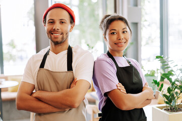 Two confident baristas smiling with arms crossed in coffee shop