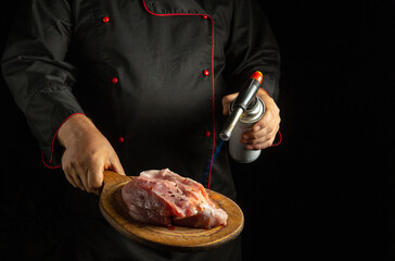 Wall Mural - Roasting raw meat with a gas burner in the chef hand. The concept of cooking a meat steak for lunch using a unique recipe.