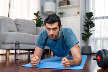 Athletic and sporty man doing plank on fitness mat during home body workout exercise session for fit physique and healthy sport lifestyle at home. Gaiety home exercise workout training.