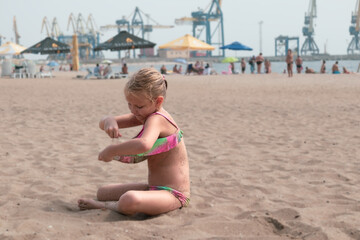 little girl 6-7 years old, blonde on the beach in a swimsuit plays with sand, sitting on the seashore