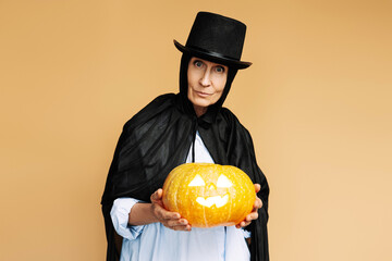 Wall Mural - Elderly woman wearing a witch costume holding a jack-o'-lantern for halloween