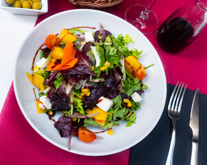 Wall Mural - Colorful salad of fresh lettuce and arugula leaves with ripe tomatoes, chopped mango, soft cheese and balsamic sauce.