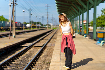 Wall Mural - Young Asian woman enjoy outdoor lifestyle road trip travel by railway transportation on summer holiday vacation. Attractive girl standing by railroad track during waiting for train at railway station.