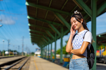 Wall Mural - Young Asian woman enjoy and fun outdoor lifestyle road trip travel by railway transportation on summer holiday vacation. Attractive girl listening to the music with earphones during waiting for train.