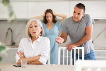 Wall Mural - Couple of adult man and woman during family quarrel with elderly woman in kitchen