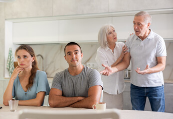 Wall Mural - Portrait of an offended married couple in a home kitchen, which mature family members reprimand. Family conflict