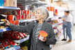 © JackF - Positive senior lady looking in local supermarket for ingredients to prepare delicious authentic Asian meals, holding colorful plastic cups with traditional instant ramen