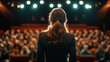 © 沈军 贡 - A woman with long hair stands on the stage of an auditorium and delivers her speech to the audience