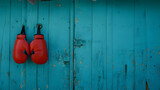 A pair of red boxing gloves hang from a hook on a weathered blue wooden wall, offering a striking contrast in color and texture, with ample copy space on the right side of the image.