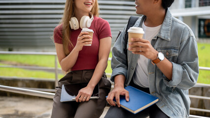 Wall Mural - Two cheerful Asian college students are enjoying a conversation outdoors while having coffee.