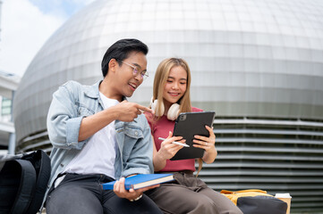 Wall Mural - Two cheerful Asian college students are having a good conversation while relaxing outdoors on campus