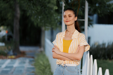 Wall Mural - Young woman standing confidently in a bright yellow top and striped shirt, smiling outdoors Natural background with greenery adds freshness Bright and cheerful atmosphere